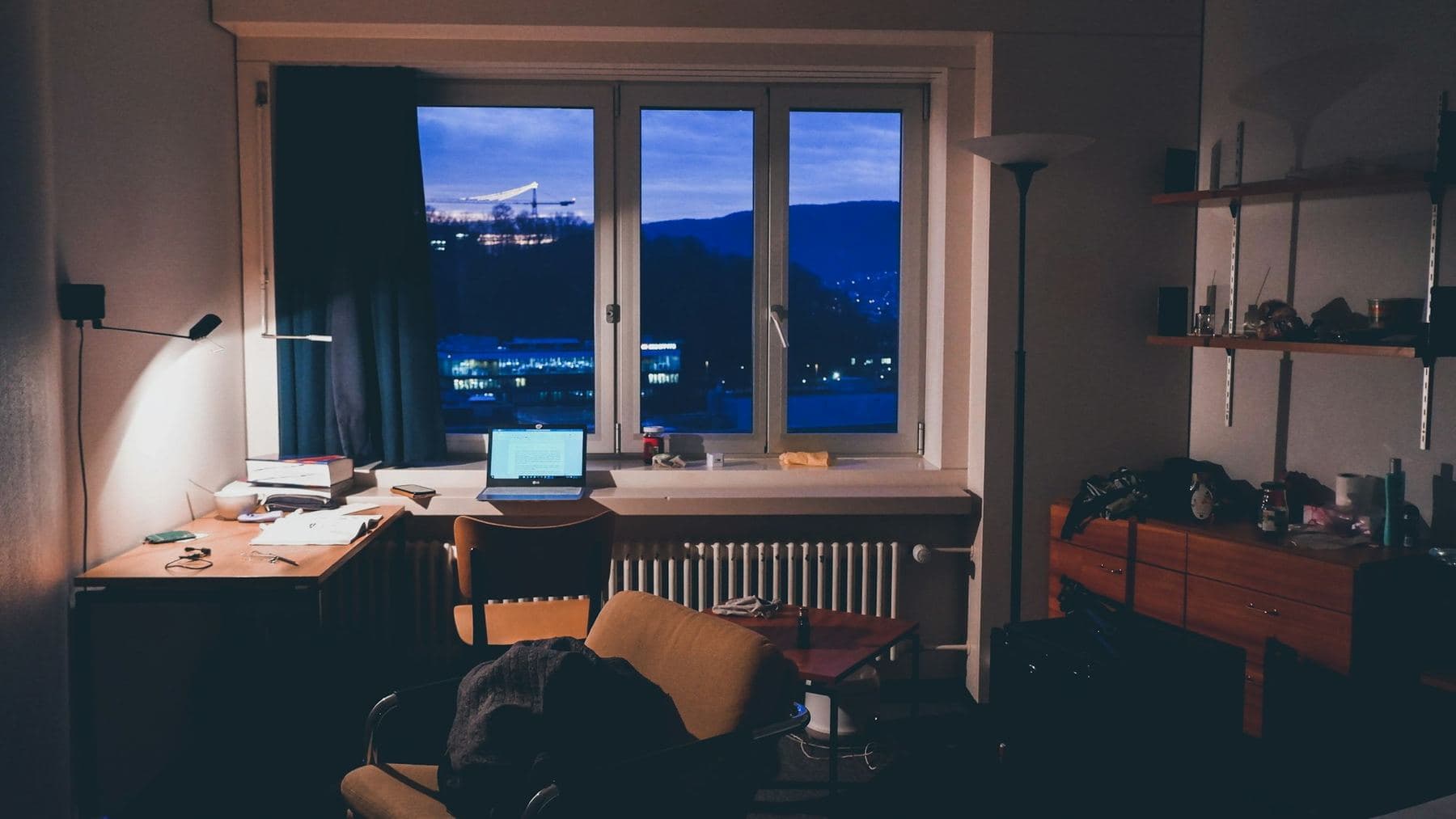 A desk at night with a laptop open in front of a window over the city